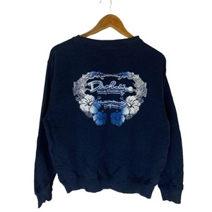 Op de afbeelding: Een donkerblauw sweatshirt met een wit bloemenontwerp en de tekst "DaKine Long Beach Huntington Beach California" op de rug.