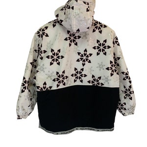 May include: White hooded jacket with a black and silver snowflake pattern. The jacket has a black waistband with the word "Courr&egrave;ges" repeated along the bottom.