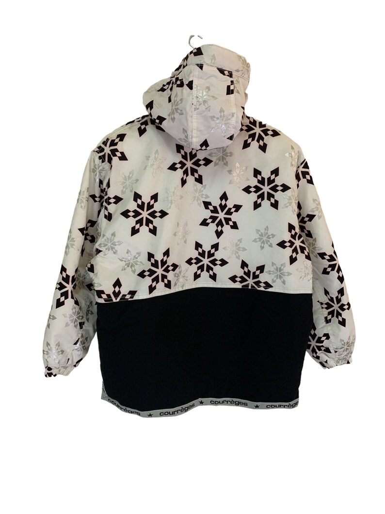 May include: White hooded jacket with a black and silver snowflake pattern. The jacket has a black waistband with the word "Courr&egrave;ges" repeated along the bottom.