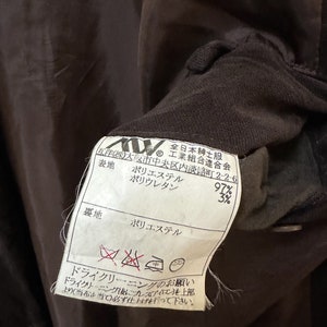 May include: A brown fabric label with white text and symbols. The label states "Polyester 97%, Polyurethane 3%" for the fabric composition. It also includes care instructions for dry cleaning only.