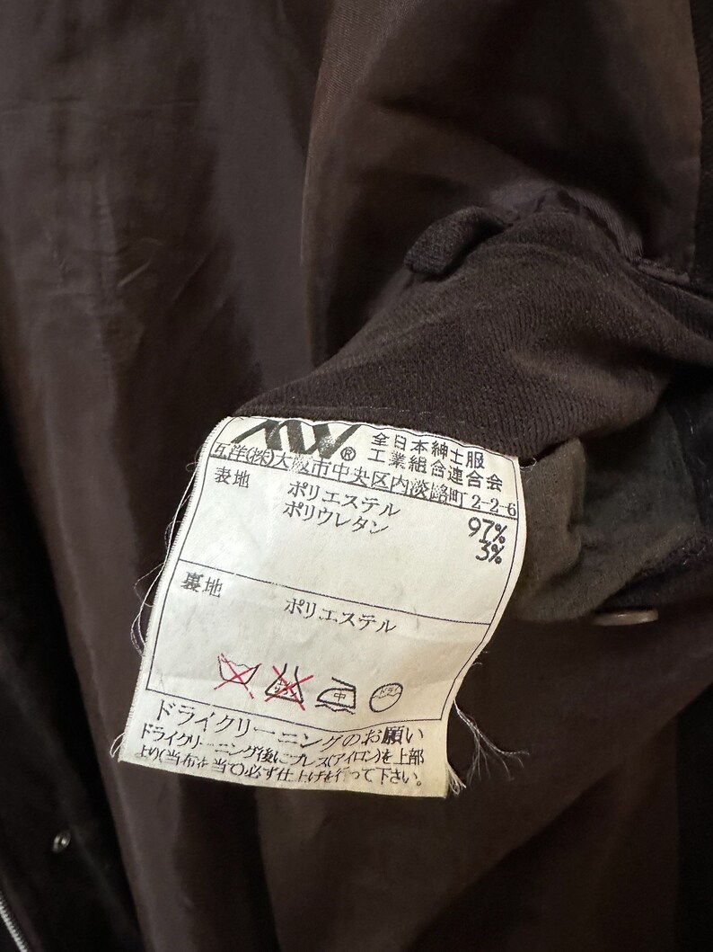 May include: A brown fabric label with white text and symbols. The label states "Polyester 97%, Polyurethane 3%" for the fabric composition. It also includes care instructions for dry cleaning only.