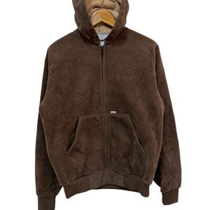 Puede incluir: Una chaqueta marr&oacute;n con capucha y cremallera, con forro de polar. La chaqueta tiene un bolsillo canguro y una etiqueta de la marca en el pecho izquierdo.