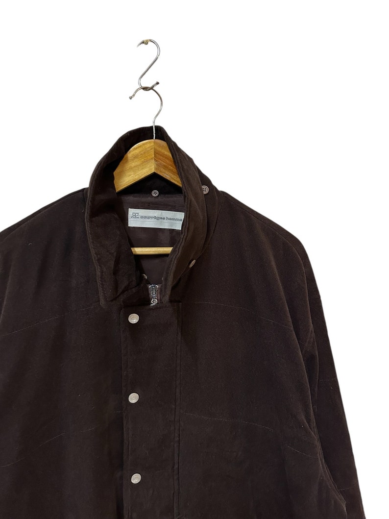 May include: A brown corduroy jacket with a zip fastening and button details. The jacket has a label that reads "comme des garcons homme."