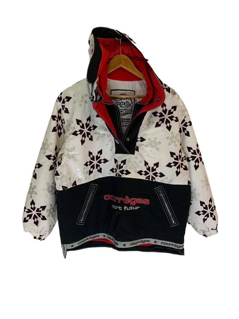 May include: White and black ski jacket with a snowflake pattern. The jacket has a black zipper and a red lining. The text "Courr&egrave;ges Sport Futur" is printed on the front of the jacket.