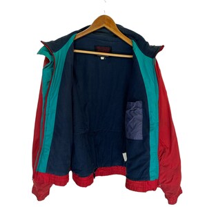 May include: A red, teal and navy blue jacket with a zip closure. The jacket has a small pocket on the inside. The label on the jacket reads "Warm Up".