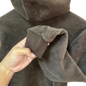 Puede incluir: Una sudadera con capucha marr&oacute;n de textura suave y peluda. La sudadera tiene una capucha con cord&oacute;n y un pu&ntilde;o de canal&eacute; en la manga.