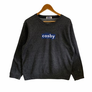 May include: A dark grey sweatshirt with a blue and white logo that says "Cosby" on the front.