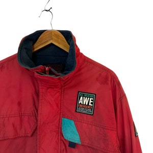 May include: Red jacket with a blue and teal pocket and a patch that says "All Weather AWE Emergency" with a logo underneath.