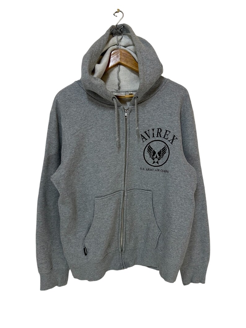 May include: A gray zip-up hoodie with a black embroidered logo that says "AVIREX U.S. ARMY AIR CORPS".