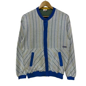 May include: A vintage, light gray bomber jacket with vertical stripes in blue and yellow. The jacket features a blue collar, button closure, and pocket accents. The brand logo is visible on the chest.