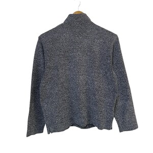 May include: A textured, dark gray sweater with a high collar and long sleeves. The fabric has a speckled pattern, and the garment is hanging on a wooden hanger against a white background. The sweater appears to be a casual, everyday wear item.