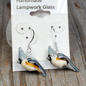 May include: Handmade lampwork glass earrings featuring a bird design with blue, white, and orange colors. The earrings are on a white card with the text "Handmade Lampwork Glass".