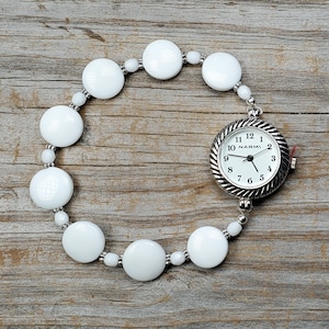 Puede incluir: Pulsera de cuentas blancas con un reloj plateado adjunto. La esfera del reloj es blanca con agujas negras y n&uacute;meros negros. La esfera del reloj dice "NARMI" en la parte superior.