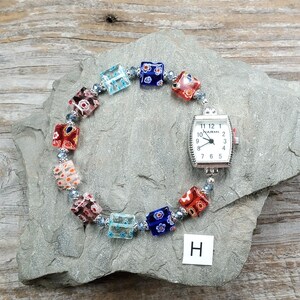 May include: A wristwatch with a rectangular silver-tone case and a white dial featuring the brand name Narmi. The watch band is composed of multi-colored square glass beads with floral patterns, separated by small silver-tone spacer beads.