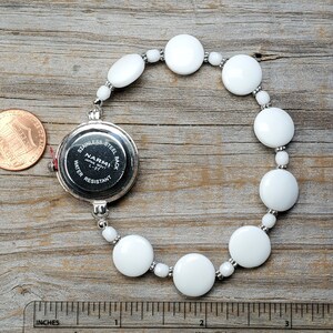 Puede incluir: Reloj de pulsera con brazalete de cuentas de cer&aacute;mica blanca y una esfera plateada que dice "NARMI JAPAN MVT L-37 WATER RESISTANT STAINLESS STEEL BACK".