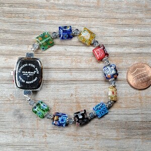May include: A wristwatch with a square stainless steel back labeled NARMI Japan Movt Water Resistant, attached to a bracelet of multi-colored square millefiori glass beads and small clear spacer beads, shown next to a copper one-cent coin.