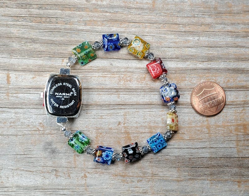 May include: A wristwatch with a square stainless steel back labeled NARMI Japan Movt Water Resistant, attached to a bracelet of multi-colored square millefiori glass beads and small clear spacer beads, shown next to a copper one-cent coin.