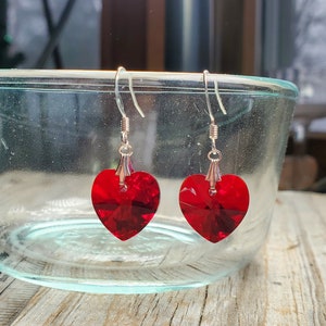 May include: A pair of silver heart-shaped earrings with red crystal accents.