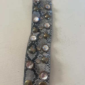 May include: A grey and black snakeskin-patterned bracelet with gold and clear rhinestones.