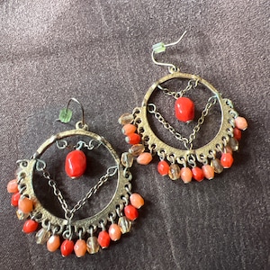 Könnte beinhalten: Ein Paar Creolen mit einer baumelnden Kette und korallenfarbenen Perlen. Die Ohrringe sind aus goldfarbenem Metall und haben einen Boho-Stil.