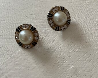 May include: A pair of silver tone earrings with a white pearl center and a black and white geometric design around the pearl. The earrings are set with clear rhinestones.