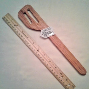 Könnte beinhalten: Ein Holzspatel mit zwei Löchern im Kopf. Der Spatel ist 28 cm lang und aus hellem braunem Holz gefertigt. Ein weißes Etikett ist am Spatel befestigt mit dem Text "Cherpt-Cregta King Two-Hole Mini Spatula - Hand-Made with Maple - #159"