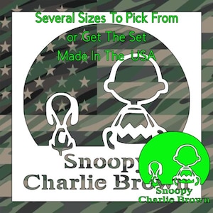 May include: A white stencil featuring the outlines of Snoopy and Charlie Brown against a camouflage background. Text reads: Several Sizes To Pick From or Get The Set, Made In The USA, and Snoopy Charlie Brown. A green circle icon is included.