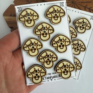 May include: A sheet of 10 wooden mushroom buttons with a smiling face and two eyes. The buttons are arranged in two rows of five. The text "FOR YOUR" and "YARNS AND LO" is visible at the bottom of the sheet.