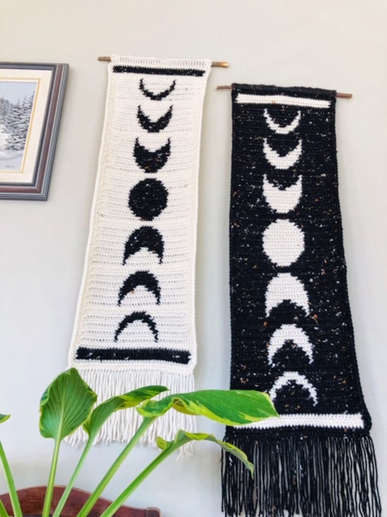 Puede incluir: Dos tapices de pared de crochet con un dise&ntilde;o de fase lunar. Uno es blanco con lunas negras y el otro es negro con lunas blancas.