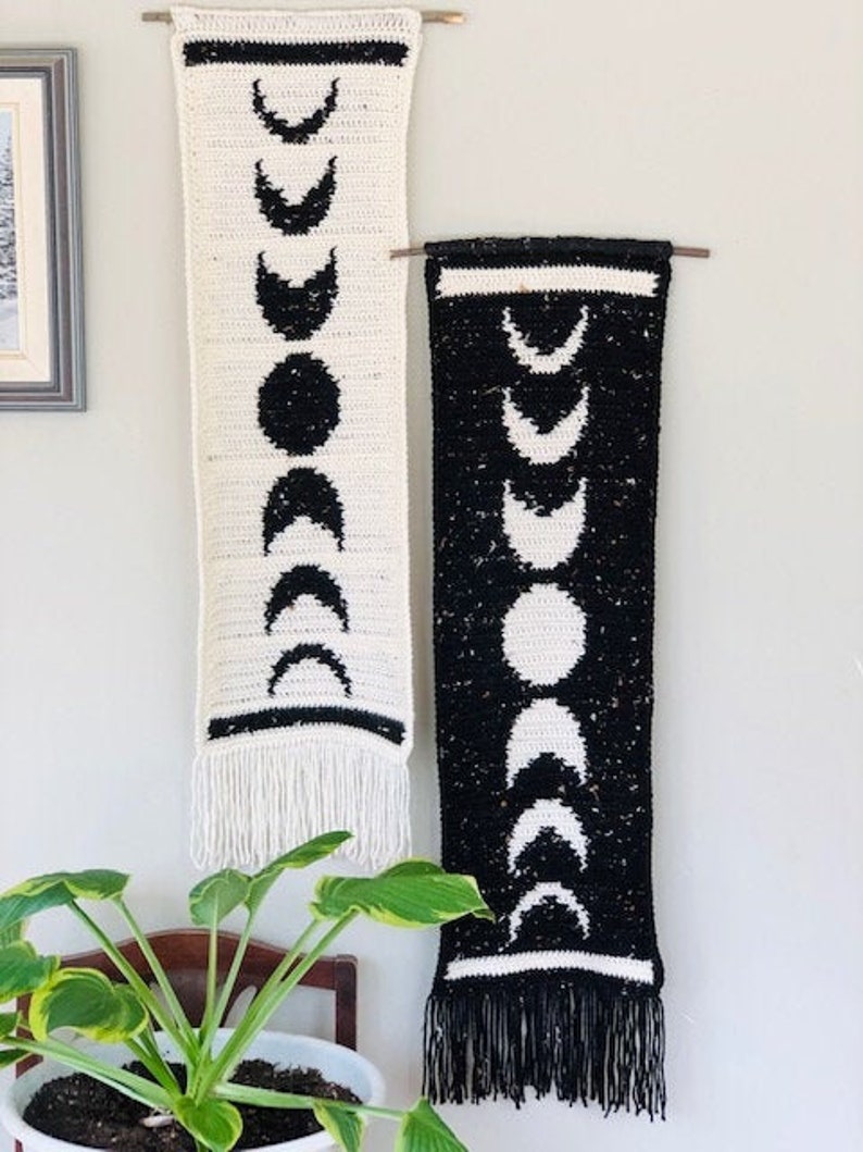 Puede incluir: Dos tapices de pared de crochet blanco y negro con flecos. Cada tapiz presenta un patr&oacute;n de lunas crecientes.