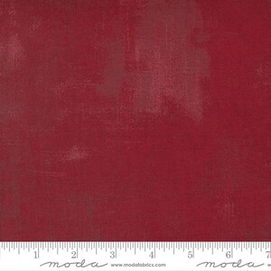 May include: A solid red fabric with a subtle textured pattern. The fabric is a deep red color with a slight sheen. The fabric is shown with a ruler for scale.