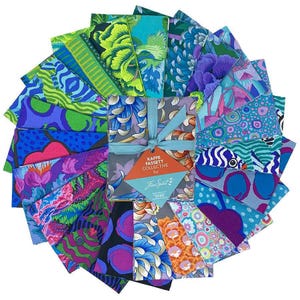 May include: A collection of colorful fabric squares arranged in a circular pattern. The fabrics feature various floral and abstract designs in shades of blue, green, purple, and orange. A bundle of fabric squares is tied with a blue ribbon and a tag that reads "KAFFE FASSETT COLLECTIVE for Free Spirit."