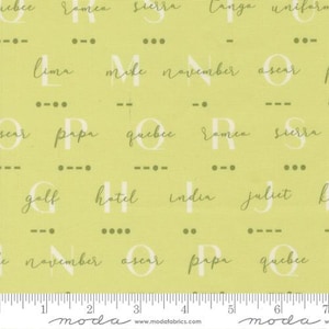 May include: A pale green fabric featuring a repeating pattern of letters and Morse code symbols. The letters are in a handwritten style and include words like "Lima," "Mike," and "Oscar." A ruler is visible along the bottom edge.