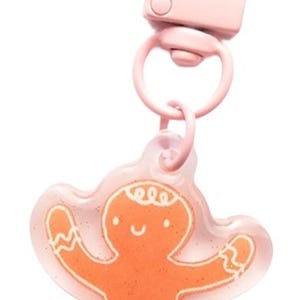 Pode incluir: Chaveiro de homem de gengibre rosa com um amuleto de plástico transparente e um fecho de metal rosa.