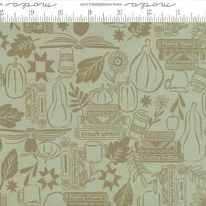 May include: A light green fabric featuring a repeating pattern of brown line drawings including stacks of books, pumpkins, gourds, leaves, flowers, and mugs. A white ruler measuring 7 inches is visible along the top edge with the text moda.