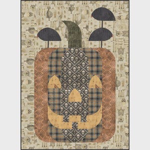 Könnte beinhalten: Ein rechteckiger Quilt mit einem zentralen Kürbismotiv aus braunen, schwarzen und beigen Stoffstücken. Der Kürbis hat eine Mitte mit Totenkopfmuster, beige Aussparungen für Augen und Mund sowie einen dunkelgrünen Stiel mit zwei schwarzen Pilzformen.