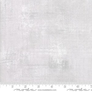 May include: A light gray fabric with a textured, distressed appearance. The fabric has a brushed effect, with visible strokes and variations in tone. A ruler is at the bottom of the fabric, with the word "moda" and the website address www.modafabrics.com.