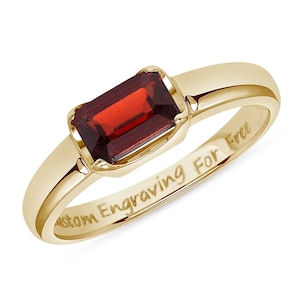 Puede incluir: Un anillo de banda de oro con una piedra rectangular roja. El interior de la banda está grabado con el texto "Grabado personalizado gratis".