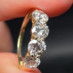 May include: A gold ring featuring four round, brilliant-cut clear stones arranged in a vertical row. The band is polished yellow gold, and each stone is secured by small metal prongs, creating a continuous line of sparkle along the finger.