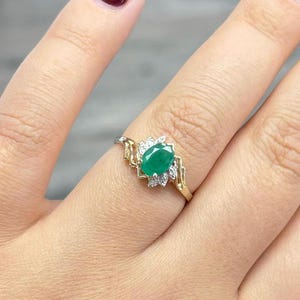 Può includere: Un anello in oro e argento con una vivace gemma verde taglio ovale, circondata da piccole pietre bianche scintillanti. Il design dell'anello include dettagli dorati decorativi sulla fascia, creando un gioiello elegante e accattivante.
