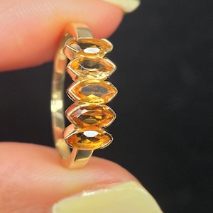 May include: A gold ring featuring five marquise-cut citrine gemstones arranged in a vertical row. The yellow-orange stones are set in a polished gold band, creating a linear design that highlights the faceted clarity of each individual gem.