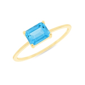 Peut inclure: Une bague en or ornée d'une pierre précieuse rectangulaire bleu clair. La pierre est sertie dans un sertissage à quatre griffes, et le corps de la bague est en or fin et poli. L'anneau est présenté sur fond blanc.
