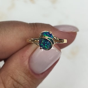 Puede incluir: Un anillo de oro con una piedra preciosa de ópalo azul y verde engastada en una banda retorcida.