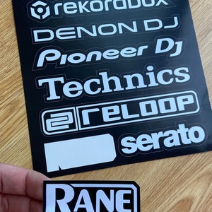 May include: A black sheet of stickers with white text. The stickers feature the logos of popular DJ software and hardware brands, including Rekordbox, Denon DJ, Pioneer DJ, Technics, Reloop, Serato, and Rane.