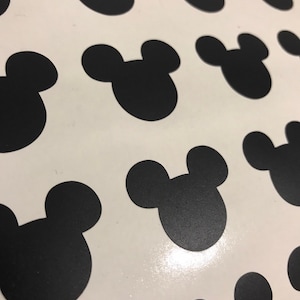 May include: A sheet of white paper with black Mickey Mouse head stickers. The stickers are arranged in a repeating pattern.