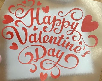Może przedstawiać: Przezroczysty, prostokątny arkusz z napisem "Happy Valentine's Day" w czerwonym skrypcie, ozdobiony kształtami serc. Para nożyczek Fiskars tytanowych, nieprzywierających z pomarańczowymi uchwytami w tle.