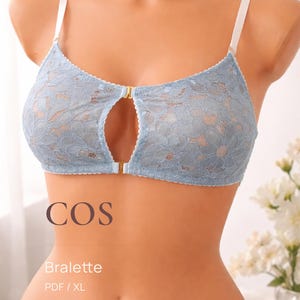 Könnte beinhalten: Hellblaue Spitzen-Bralette mit Schlüsselloch-Design und goldfarbenem Verschluss. Die Bralette hat weiße Träger und wird auf einer Schaufensterpuppe präsentiert. Das Wort "COS" ist auf der Vorderseite aufgedruckt, zusammen mit "Bralette" und "PDF / XL".