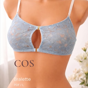 Könnte beinhalten: Hellblaues Spitzen-Bralette mit weißen Trägern und Schlüsselloch-Design. Das Bralette hat ein Blumenmuster und einen goldfarbenen Verschluss. Das Wort "COS" ist über dem Wort "Bralette" aufgedruckt.