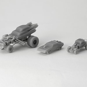 May include: Three gray toy cars, one is a large, modified truck with a large engine, one is a sleek, futuristic car, and the other is a smaller, rugged car.