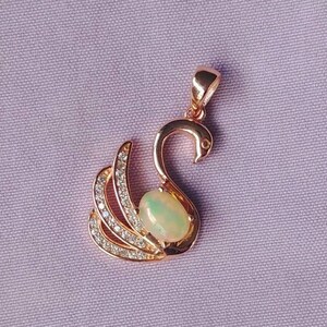 May include: A rose gold pendant featuring a swan design with a clear opal gemstone in the center. The swan's wings are adorned with small clear cubic zirconia stones.
